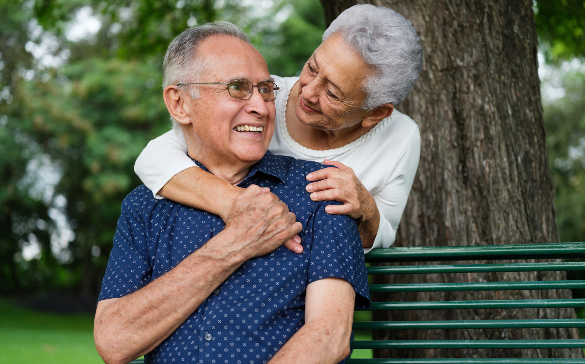elderly couple sitting and laughing together on a park bench