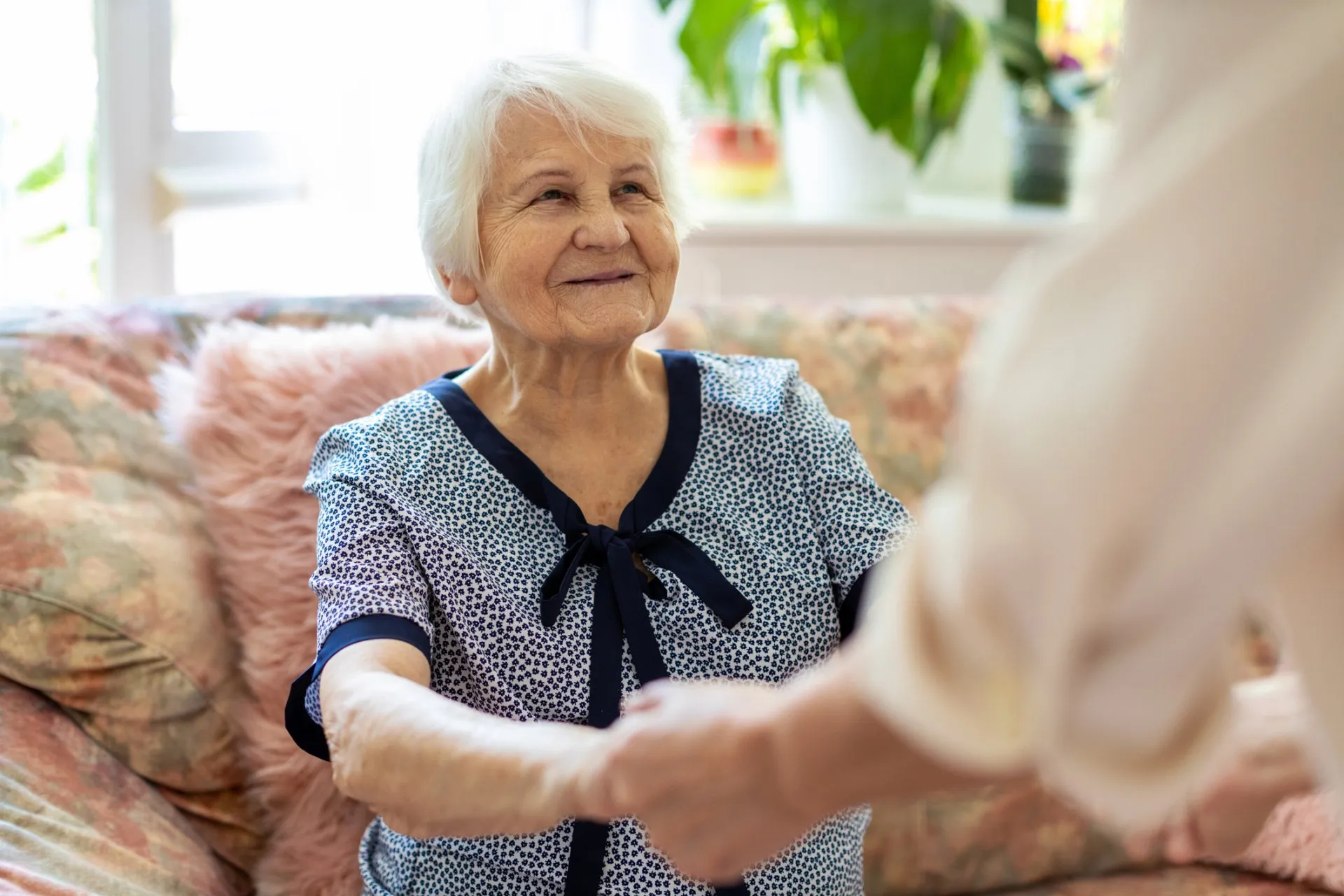 senior woman sitting on couch holding hands with somone