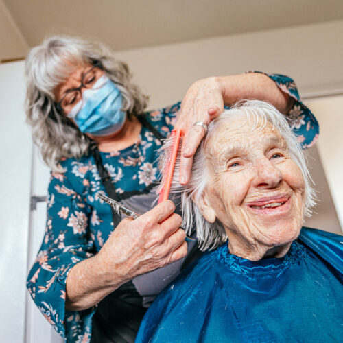 caregiver giving smiling elderly woman a haircut