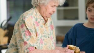 An elderly woman peeling potatoes in a kitchen with a boy looking on which answers what is home care service.