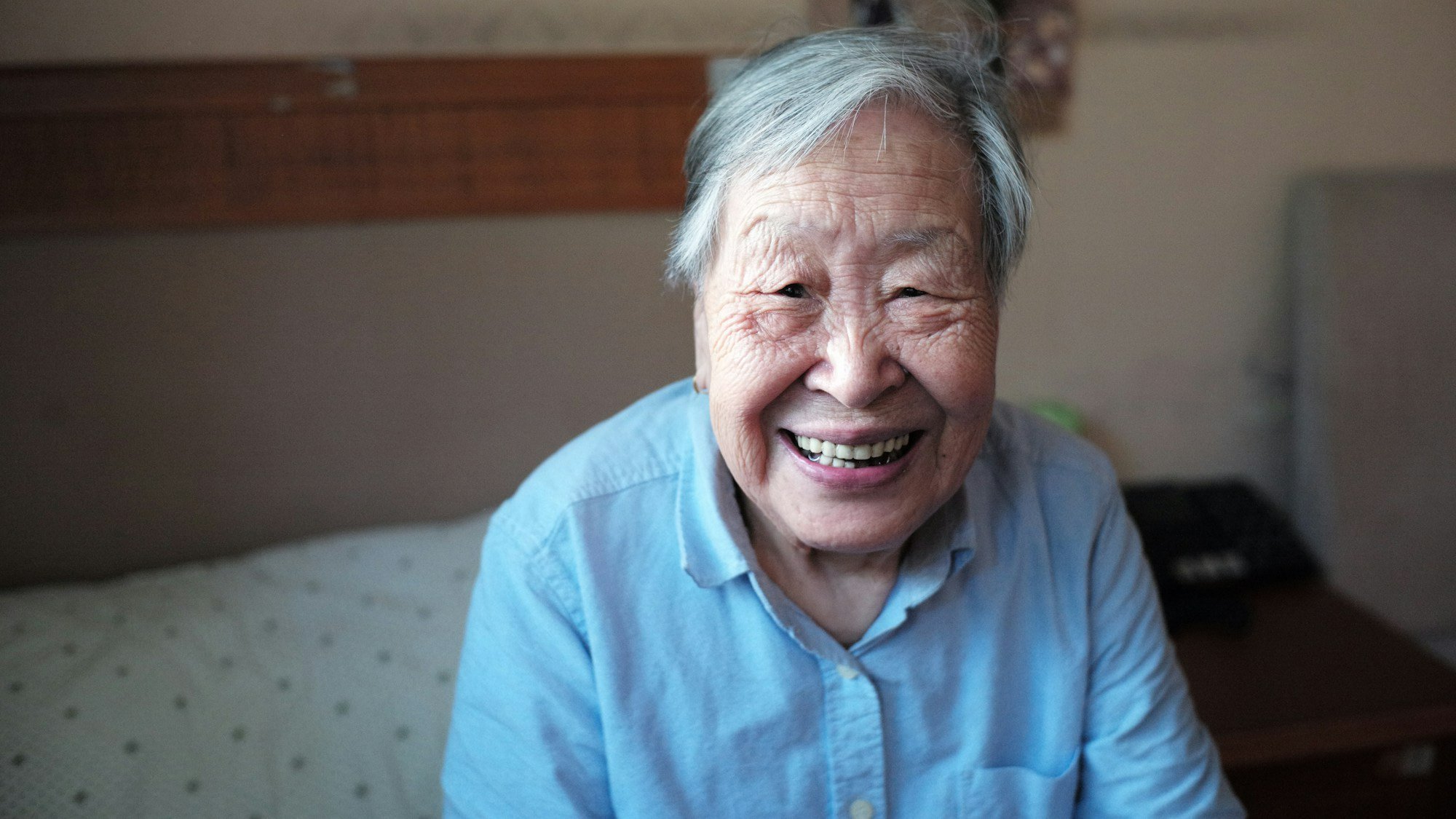 An elderly man in a blue shirt in his bedroom smiling showing the upside of caring for elderly parents.